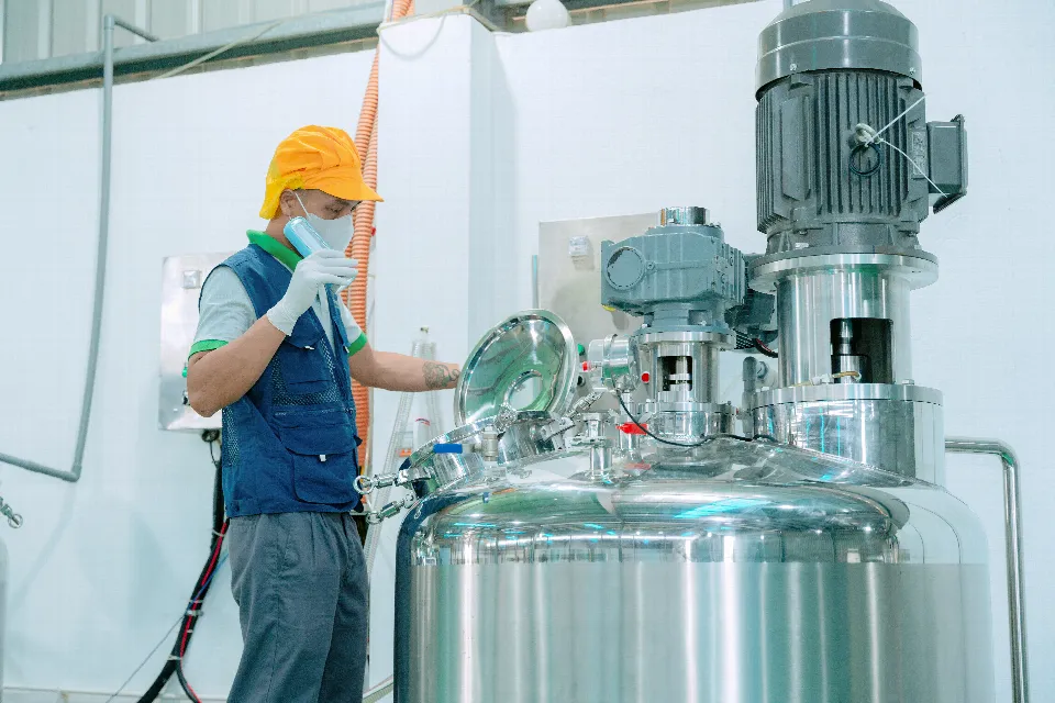 Ein Mitarbeiter mit Schutzhelm prüft einen Edelstahltank in der Fabrik