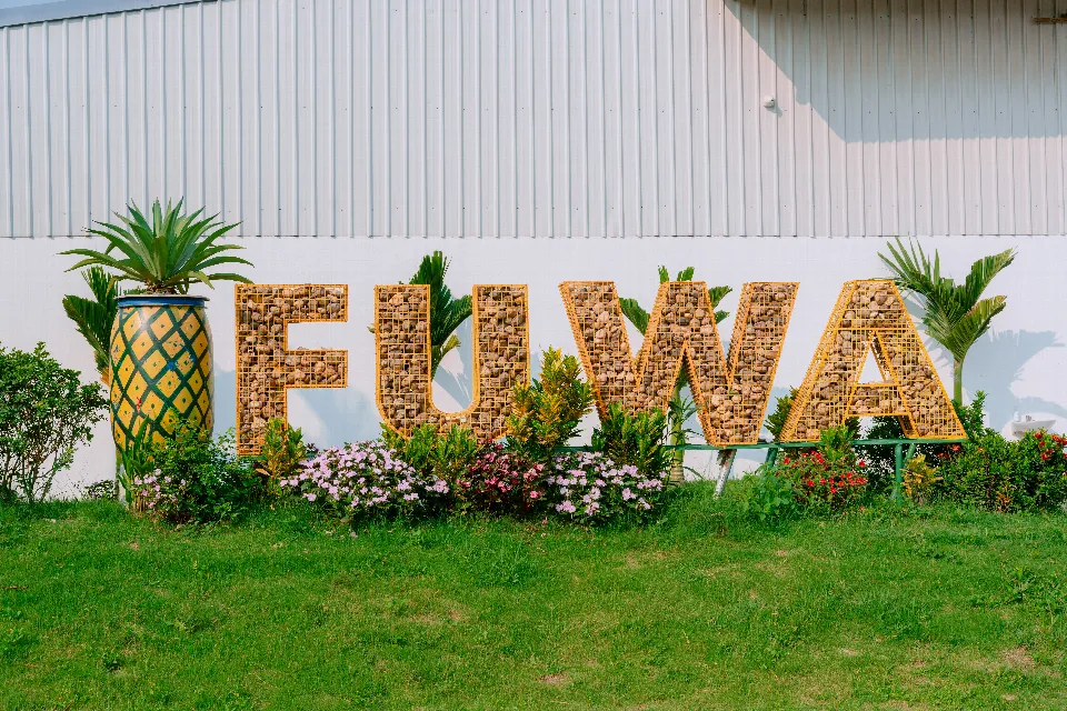 Der Schriftzug FUWA mit einer Ananasfigur im Garten vor der Fabrik