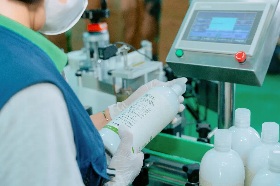 Eine Mitarbeiterin hält eine frisch etikettierte Flasche an der Etikettiermaschine